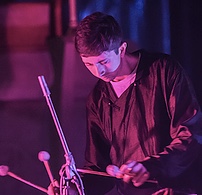 musician druming as he stands in soft purple and blue light