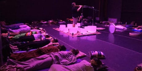 people laying down around a sound bowl musician in purple lighting