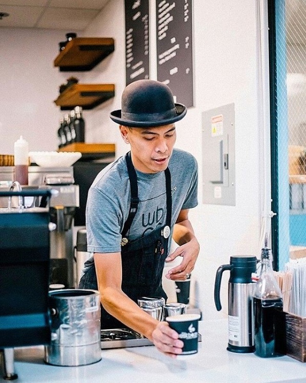 Barista with a bowlers hat serving coffee in a hipster looking cofeeshop
